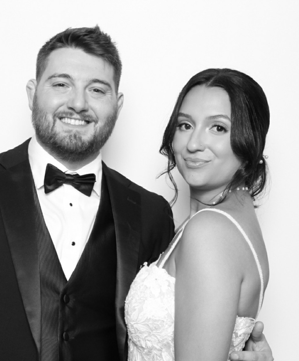 A groom in a black tuxedo and his bride in a studio lit black and white portrait